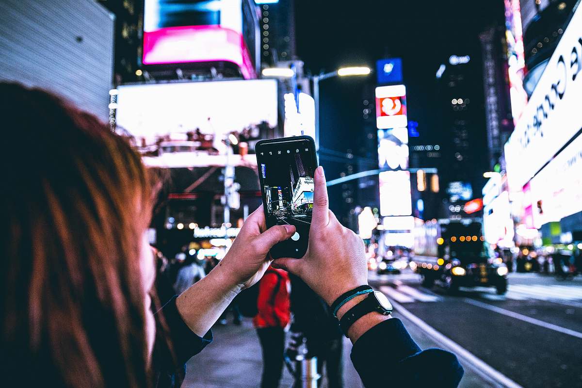 This stunning image features a woman skillfully taking a photograph of a vibrant city skyline at night using her mobile phone. The scene captures the energetic atmosphere of urban life illuminated by city lights, making it perfect for blogs, articles, or advertising campaigns focused on travel, technology, or lifestyle. Ideal for showcasing the fusion of modern technology and exploration in the heart of the city.